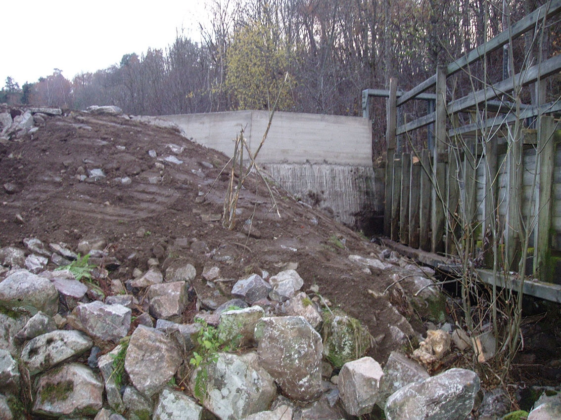 Iordningställande av marken vid dammen till Rasmus kvarn i Röttle efter kraftiga skyfall med översvämning som följd. En stödmur har gjutits vid dammfästet.