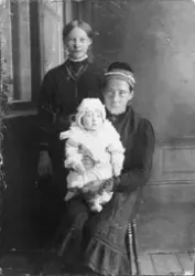 Studioportrett av ei jente og en kvinne med dåpsbarn på fang