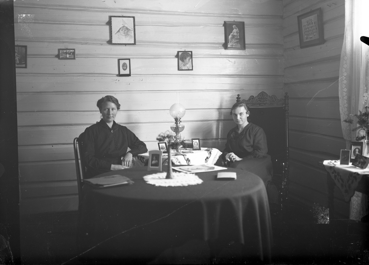 Portrett av to kvinner med interiør (2 foto). Kvinnen til høyre er antagelig lærer ettersom vi kan se henne i et klassebilde sammen med skolebarn 

Fotosamling etter fotograf og skogsarbeider Ole Romsdalen (f. 23.02.1893).