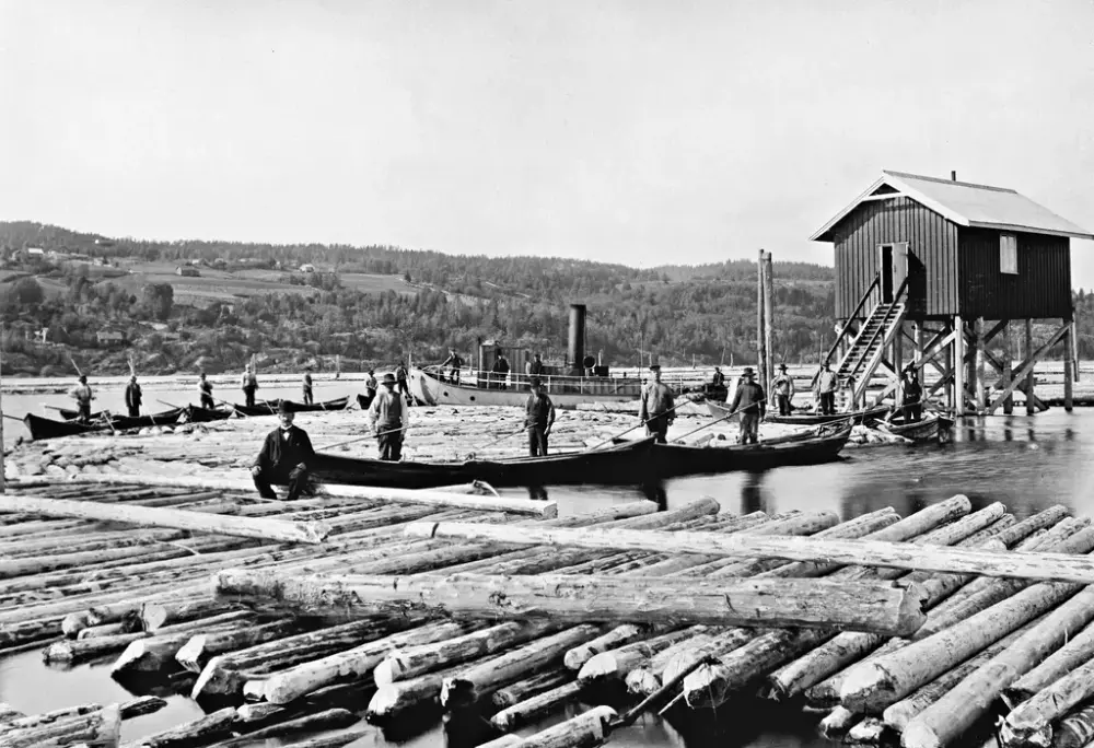 Lensearbeidere, båter, tømmer og en hvilebrakke. Vestvollen, Nordre Øyeren. Rælingen ses til venstre i bildet. Bildet er trolig tatt rundt 1930-1936. Foto: MiA-Museene i Akershus.