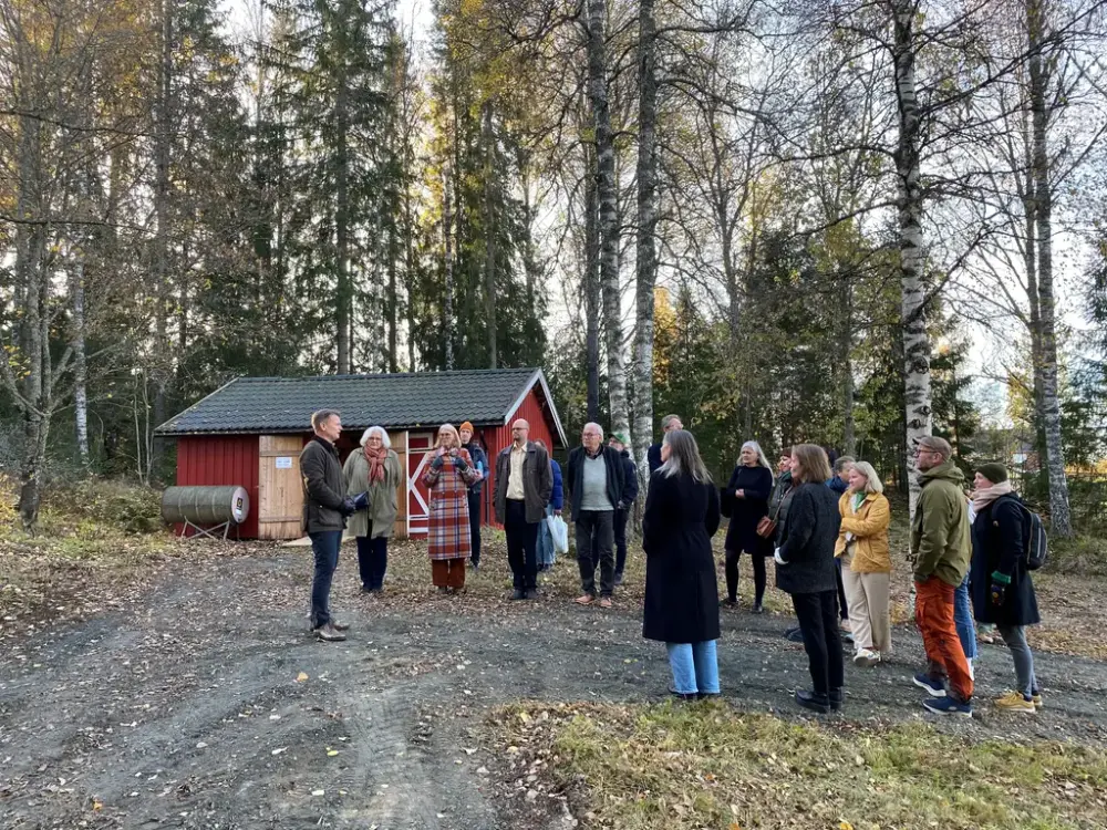 En gruppe mennesker utendørs står og hører på en mann snakke.