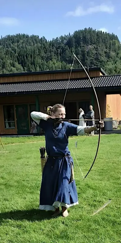 Kvinne i blå middelalderkjole som skyter med en langbue