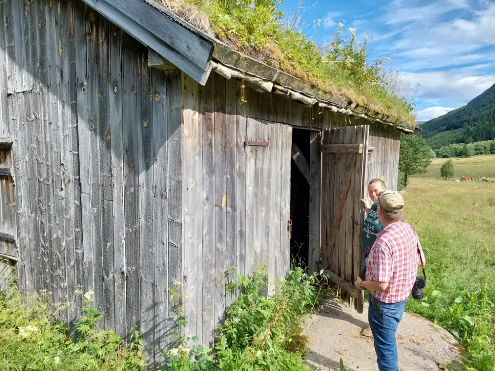 Trebygning med torvtak. To mennesker ved inngangen.