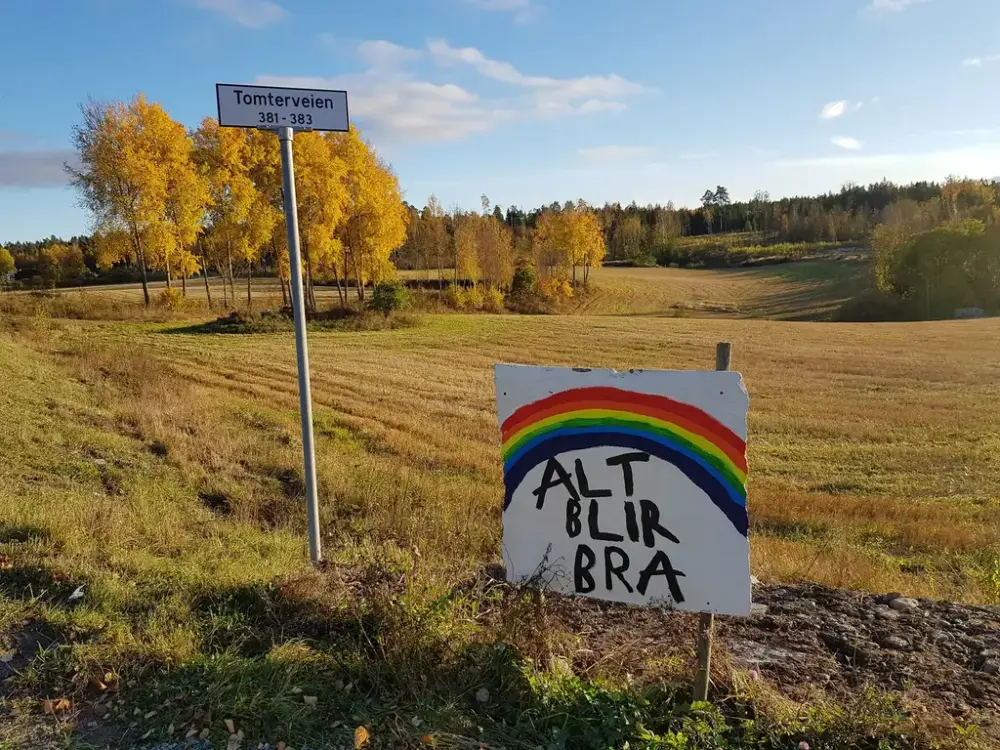 Et skilt med teksten "Alt blir bra" og en regnbue, står ved et jorde.