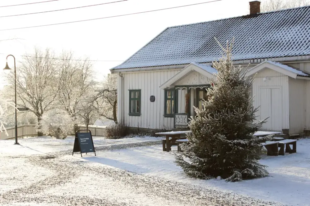 Hvitt hus i vinterlandskap med juletre med lys i forkant