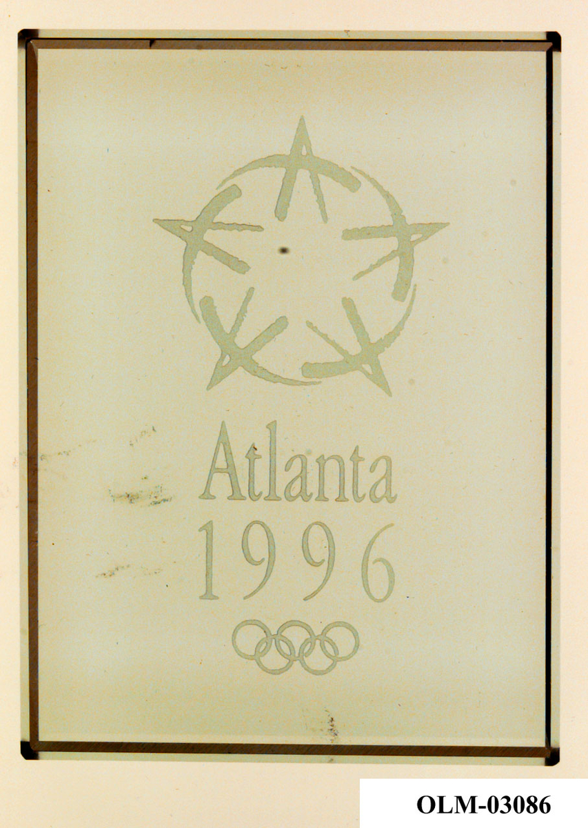 Plakett av glass med motiv av en stilisert stjerne og de olympiske ringene. 