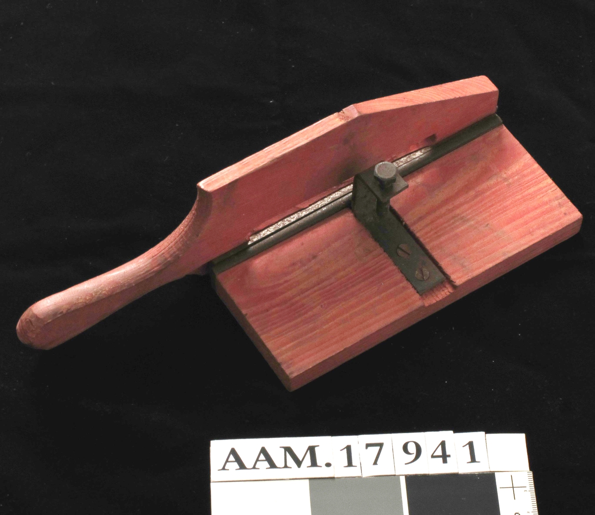Skjæremaskin for tobakk,  fra krigen 1940-45.   
Furu,  rødmalt,   jernkniv.   
Kniv uten skarp egg. Form som en papirskjærer,  med håndtak/kniv langs den ene langside. Stilleskrue pm.  Tilstand: jernet rustent. Virker lite brukt.