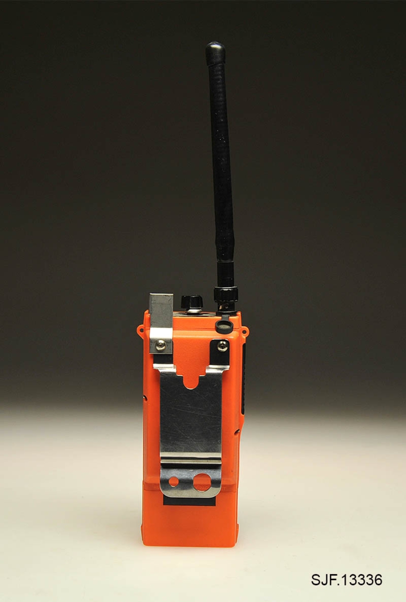Denne kommunikasjonsradioen er en Icom IC-H12 med egen batterilader (ladestasjon). Radioen har fungert både som sikringsradio i skogbruket og som jaktradio. Det er installert ekstra kanaler for jakt (jaktkanaler) som dermed har muliggjort kombinasjonsbruk, skogbruk og jakt. Sikringskanalene er merket rødt.  Radioen har en rektangulær form, oransjefargede deksler og svart antenne. På toppdekslet er det montert tre knapper og en antenne. En kapp er kanalvelger, en annen er volumknapp og en tredje knapp (rød) for nødsending er merket med SQL. SQL merket indikerer trolig en mulighet for å regulere signalets styrke før høyttaleren åpner. På siden er det en svart knapp som brukes for sending og av meldinger. Under et gummideksel ved antenna er det mulighet for tilkobling av øretelefoner og mikrofon.  På baksiden er radioen utstyrt med en metallklype (10, 5 cm lang), slik at den lar seg feste i f. eks. et belte. Batteriladeren, BC-35, som følger med til radioen er utstyrt med en 160 cm lang ledning, slik at den kan kobles til en stikkontakt (220-240 volt). 
Det er påmontert fire gummiknotter på batteriladerens bunnplate. 