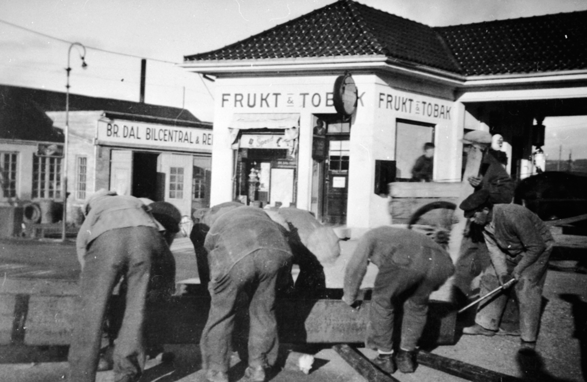 Sandbakkens Frukt & Tobakk, Furnesvegen, Brumunddal Bilcentral, bensinstasjon. Ukjente menn flytter vannledning i tre.