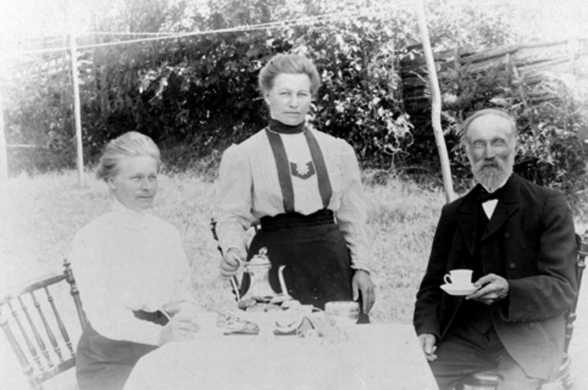 3 voksne rundt kaffebord utendørs. Fra venstre er Klara Dæhlie, Johanne Dæhlie, Gudbrand Olsen, Høiby, Nes, Hedmark.