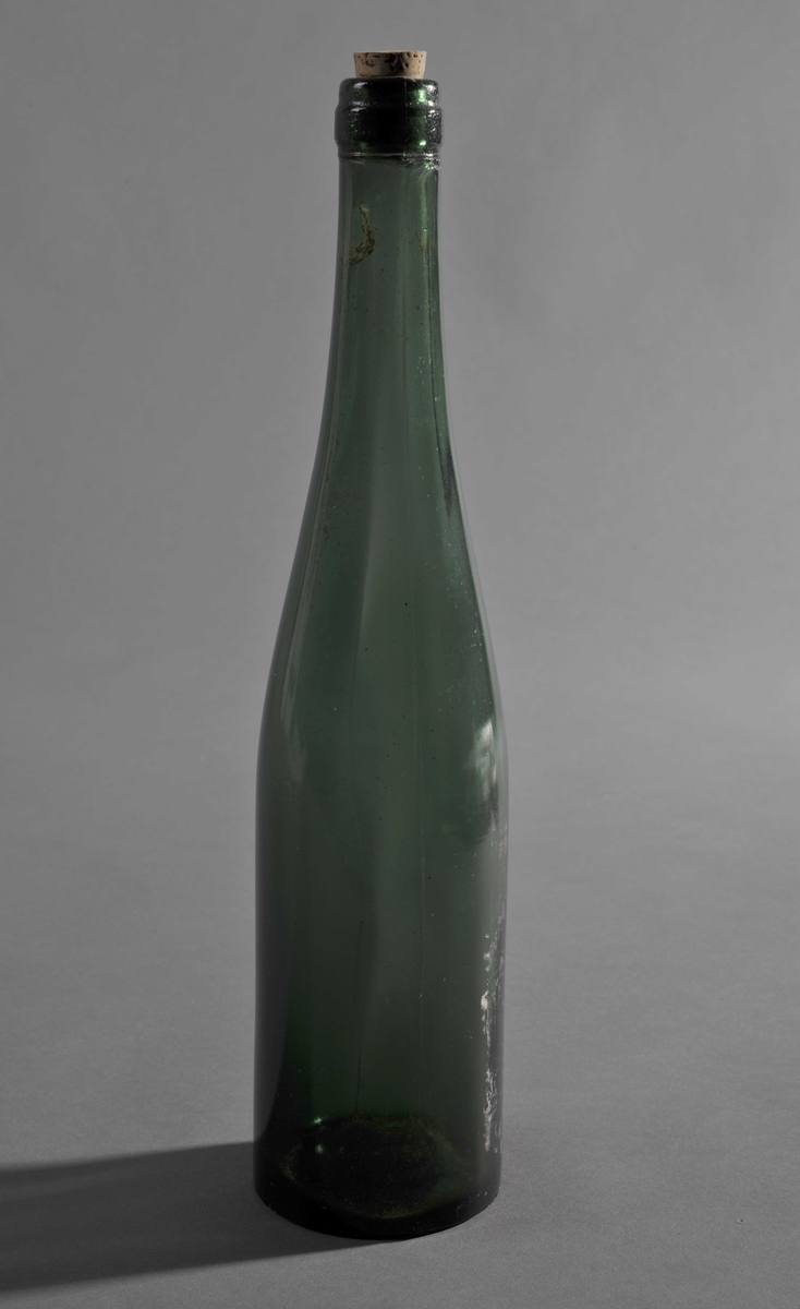 Grønn, støpt glassflaske med flat bunn. Flasken smalner gradvis fra midten av flasken til toppen. En kork sitter i munningen.