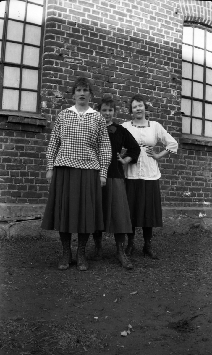 Tre ukjente kvinner foran mursteinsbygning. 