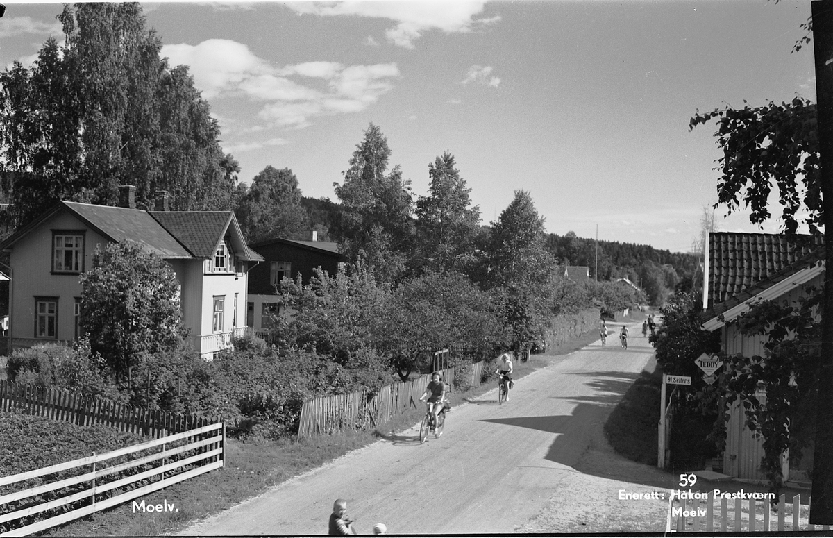 Postkort, Ringsaker, Moelv, Storgata 93, Elisenberg 378/24/13 til venstre, kiosken Knippa i Storgata 102, 378/485 til høyre, syklister på riksveg 50,