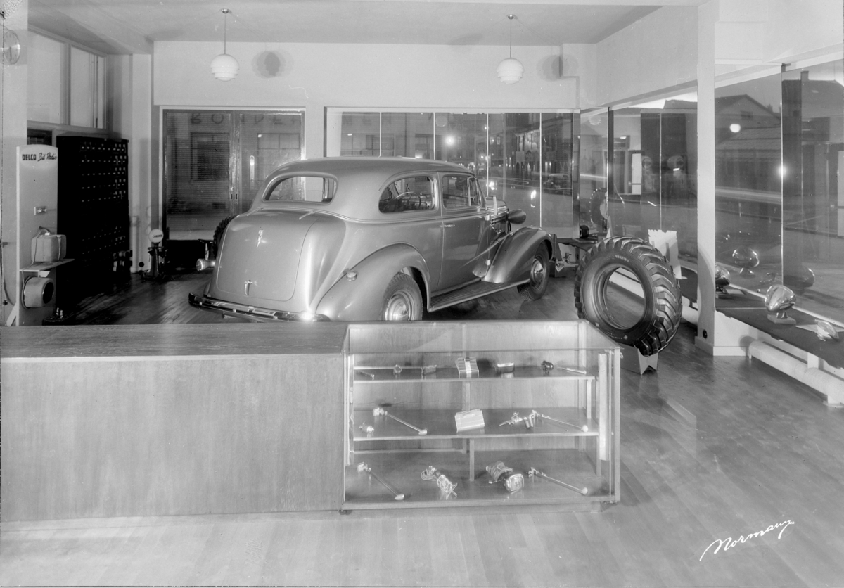Oustad Mek. Verksted A/S. Hamar. Interiør, Utstillingslokale. Bilen er en Chevrolet 1937-38. Disse to årsmodellene karakteriseres av den rette, skrånende profilen nederst på pansersiden med fortsettelse et stykke inn på døra. Bilbutikk.
