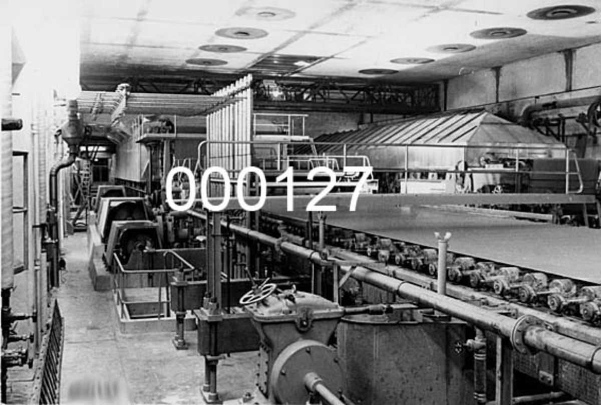 Interiør fra Drammenselvens Papirfabrikker på Geithus i Modum kommune i Buskerud.  Fotografiet viser PM IV sett fra baksida (drivsida) slik maskinen så ut etter en ombygging i 1956. 