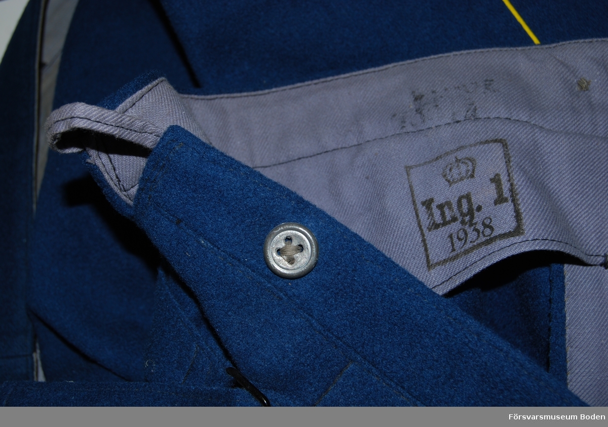 Mellanblått kläde med gul passpoal längs yttersömmarna och upp till de vertikala fickornas nederkant. Knappar av tennlegering ("blyknappar") i gylf och runt midjan. Baktill sprund med stropp för upphängning och på utsidan slejf med spänne. Byxbenen är upplagda ca 10 cm och saknar knappar för hällor. Stämplade med årtalet 1938.