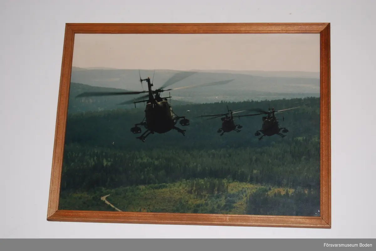 Färgfoto i ram med glas, 42 x 32 cm. Fotot är taget i luften och föreställer tre flygande helikoptrar över skog.