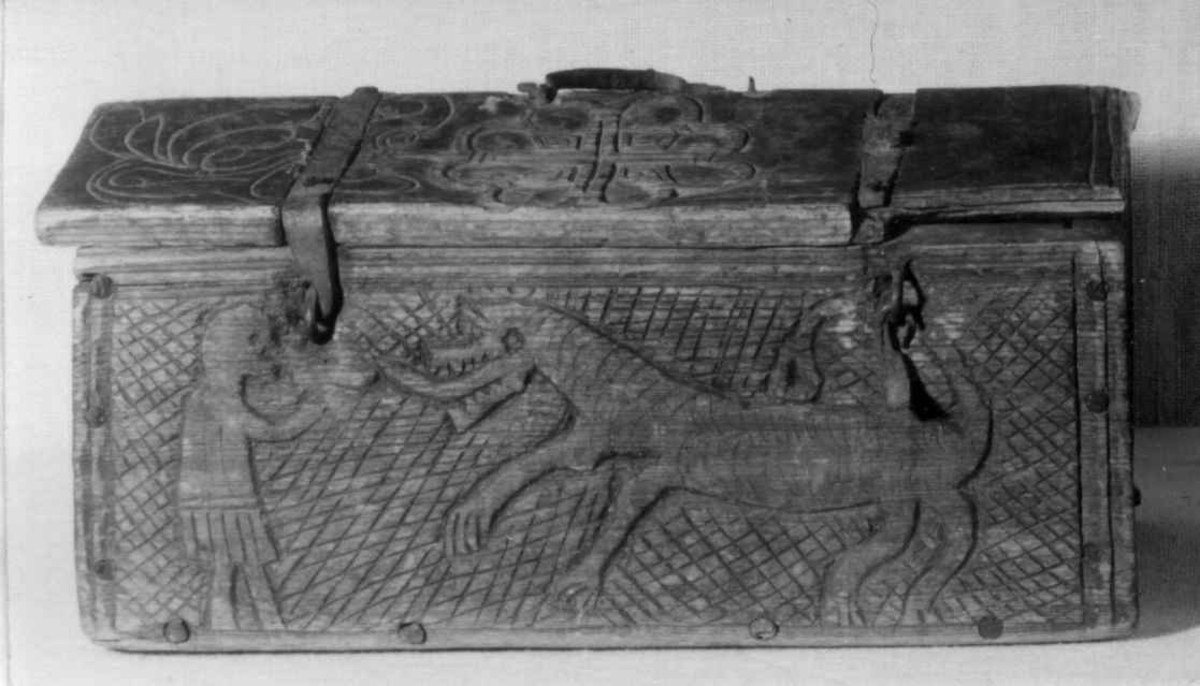 Skrin med flate sider of lett takformet lokk. Hengslet i bakkant og låsmekanisme i forkant. Håndtak midt på lokket. Hele utsidenhar skurd dekor med ranker, dyr og mennesker.