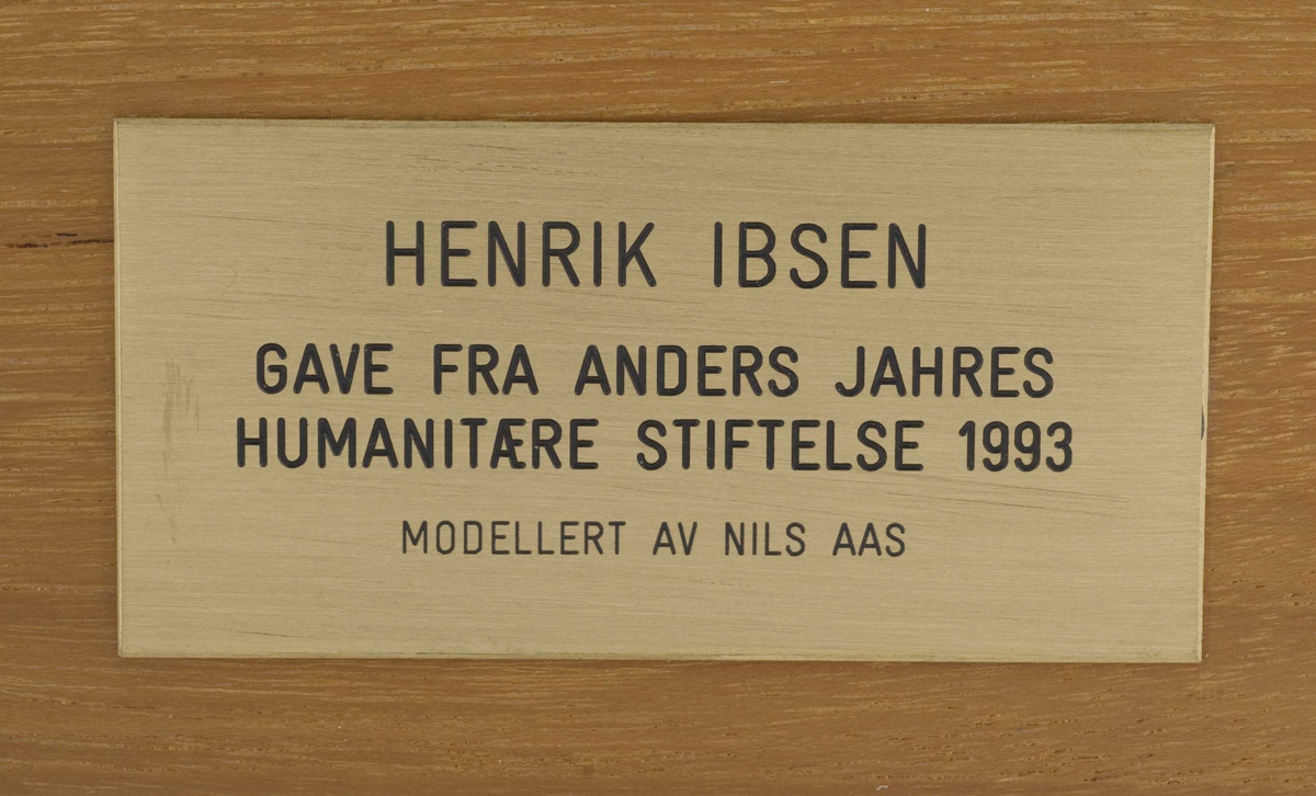 Metallskulptur på tresokkel, plakett på sokkel.