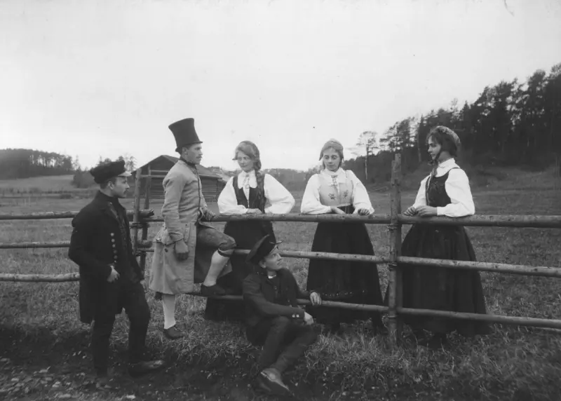 Tilstelning på Norsk Folkemuseum i 1903. Menn og kvinner samlet ved gjerdet.

Bilete er teken i samband med fyrste særutstillinga ved Norsk Folkemuseum, "Nationaldragter", og motivet er drakter frå Gudbrandsdalen. Ragnhild Prestgard står som nr. tre frå venstre.