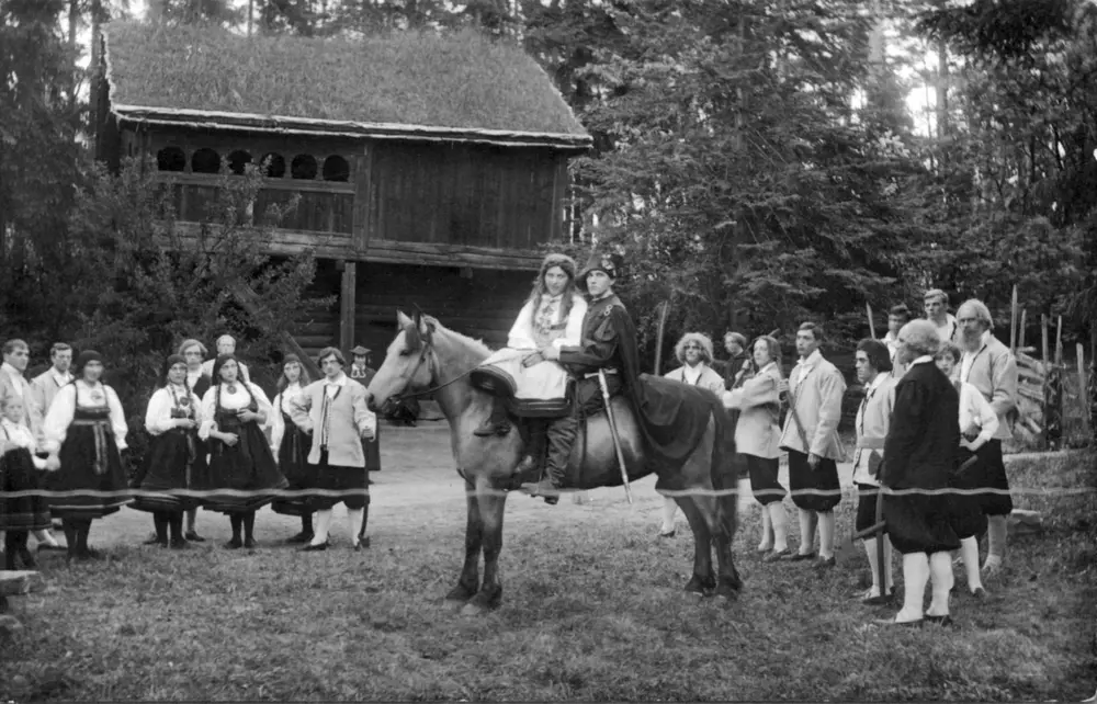 St. Hans feiring på Norsk Folkemuseum i 1916. Forestillingen «Bruderanet« framføres foran Rolstadloftet. Aktører i kostymer, deriblant et par på hest.