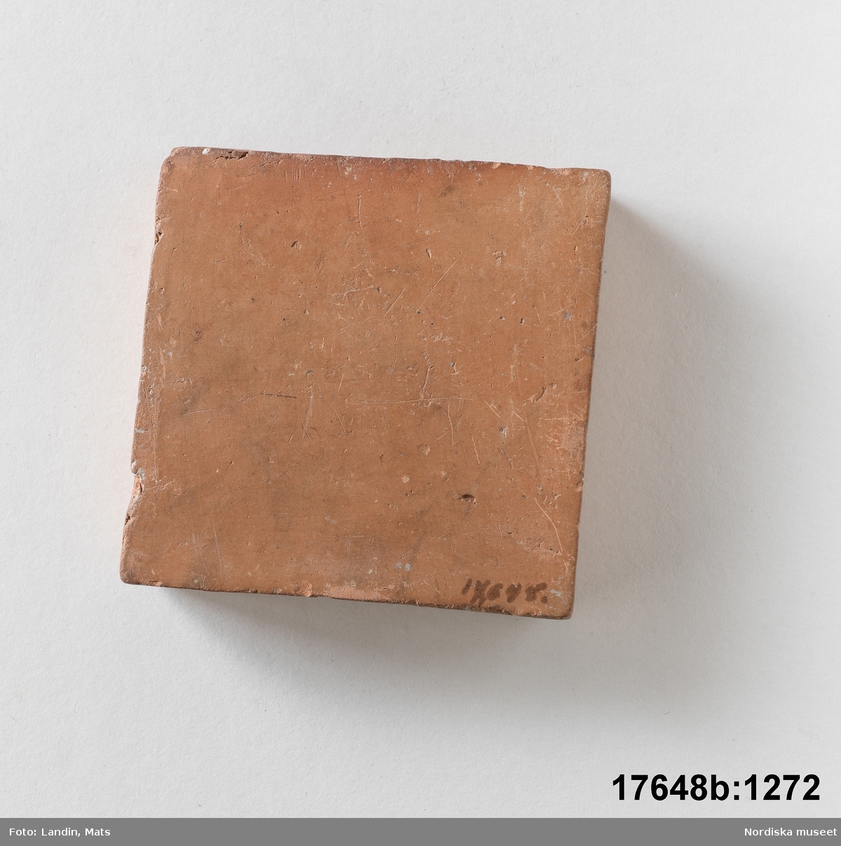 Kvadratisk platta av bränd oglaserad röd lera. På en sida text: "Bränd men oglaserad".
/Leif Wallin 2014-01-07