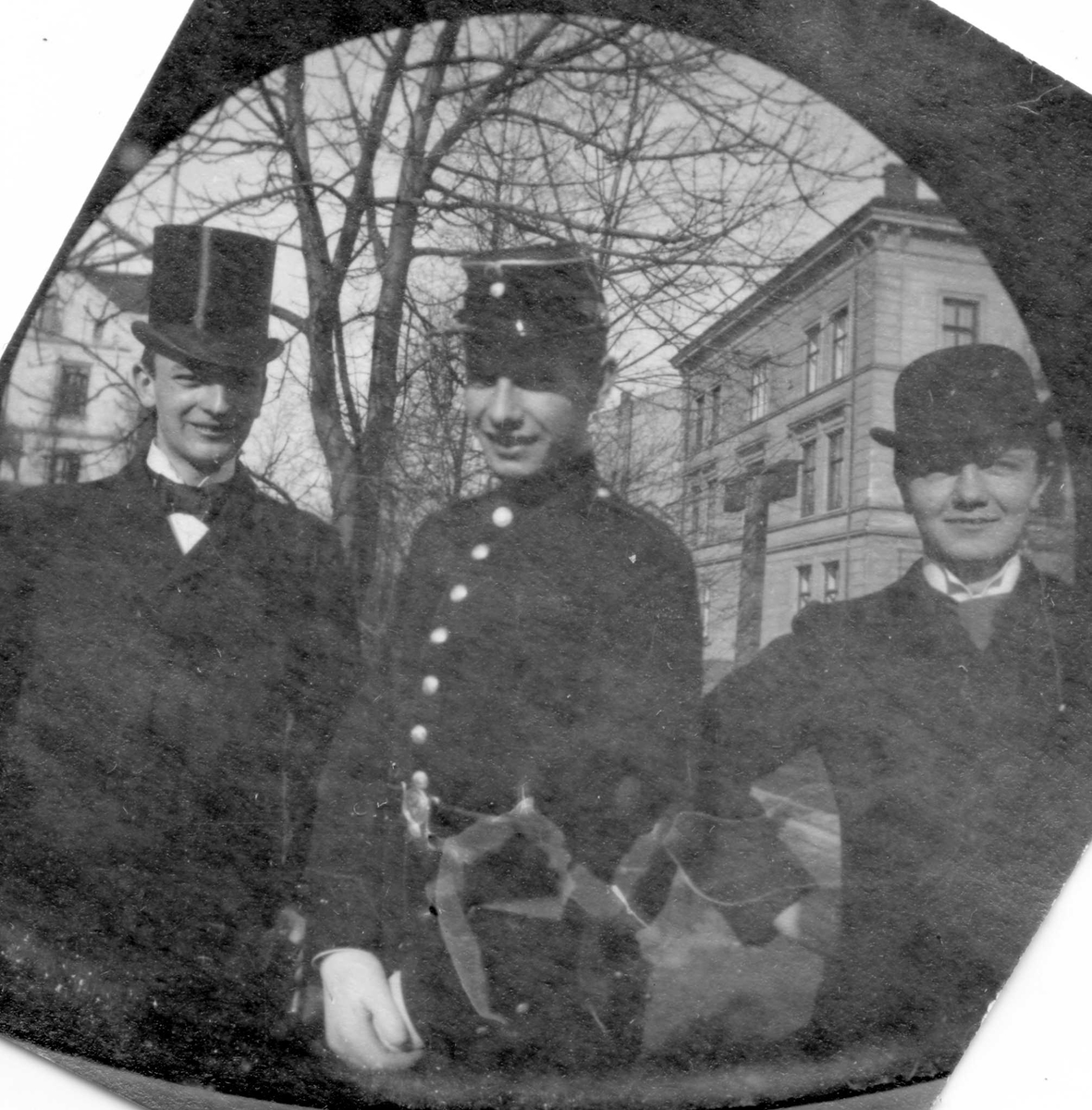 Tre menn i bygate, en med flosshatt og en i uniform.