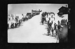 Hopprenn. Hopper i svevet. Skiløpere står langs unnarennet. 