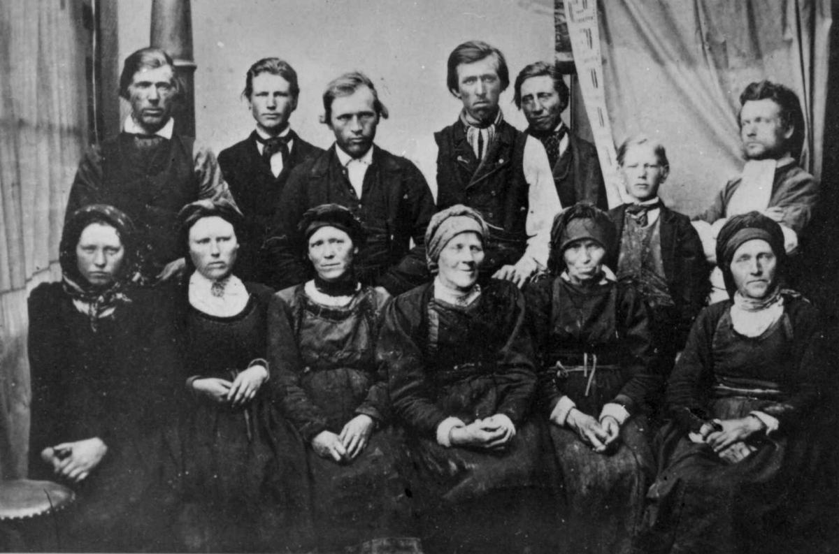 Gruppe husmenn med koner og mødre på gården Moen, Kviteseid, eid av propietær og landhandler Christian Munthe (1818-92), som også har tatt bildet. 