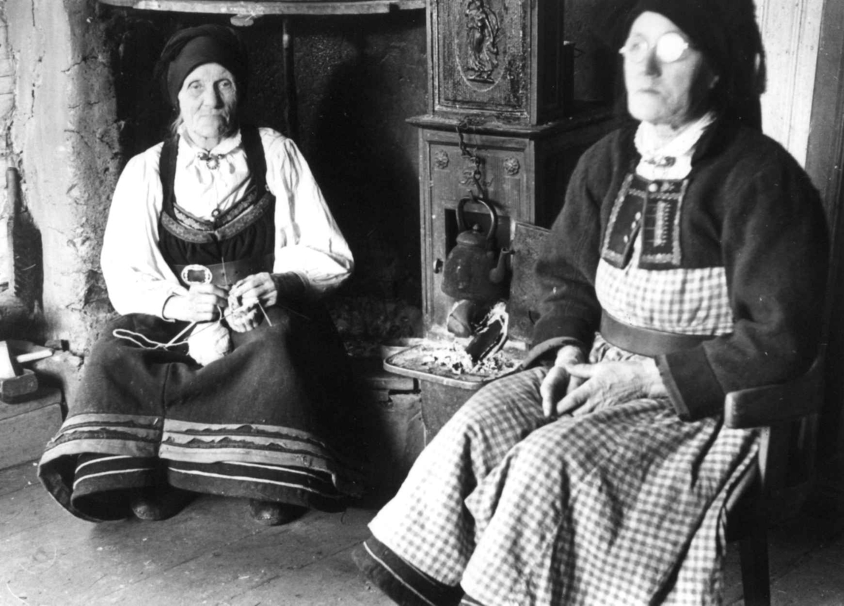 Valle, Aust-Agder 1938. Kaffekoking. To kvinner sitter ved grua.  
Vanlege klæde ein kjøleg haustdag.
Kaffi-<kasle> kokar. < Kaffi-tron> har nett vore brukt.
Frk. Ingeborg Skeivollen, Valle.