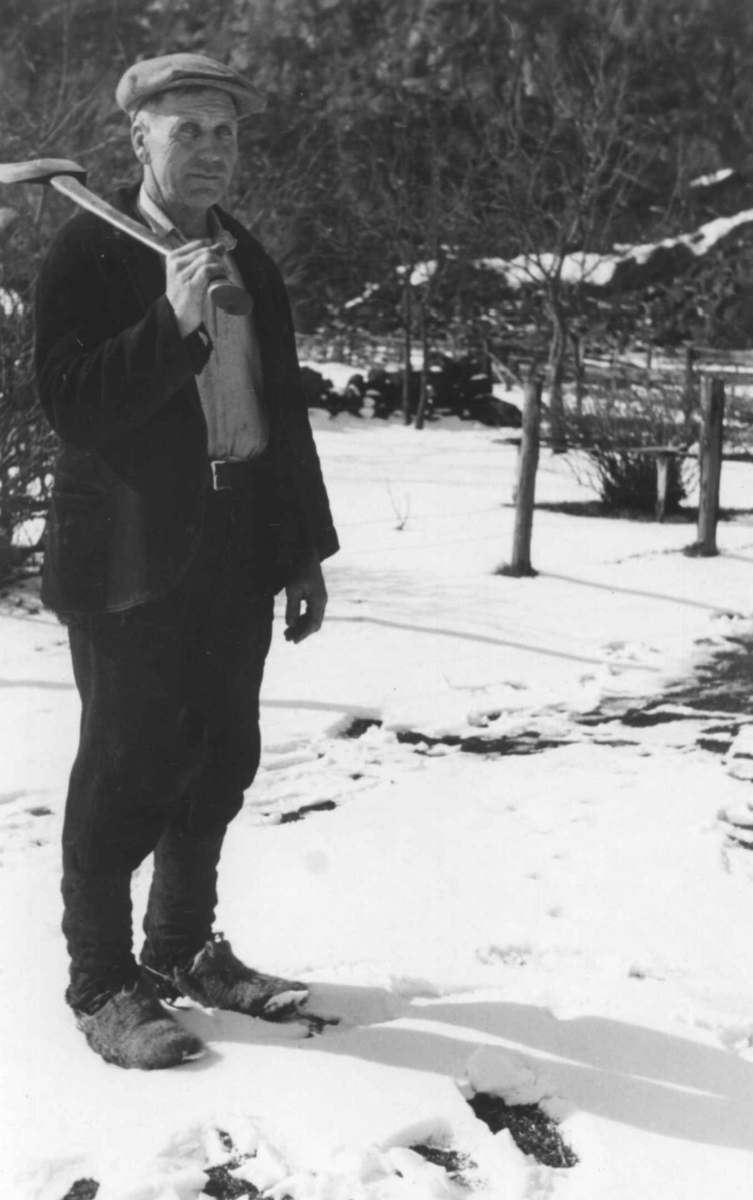 Jakob Smeland med snøsokkar og lodder holder en øks på skulderen. Åseral 1943.