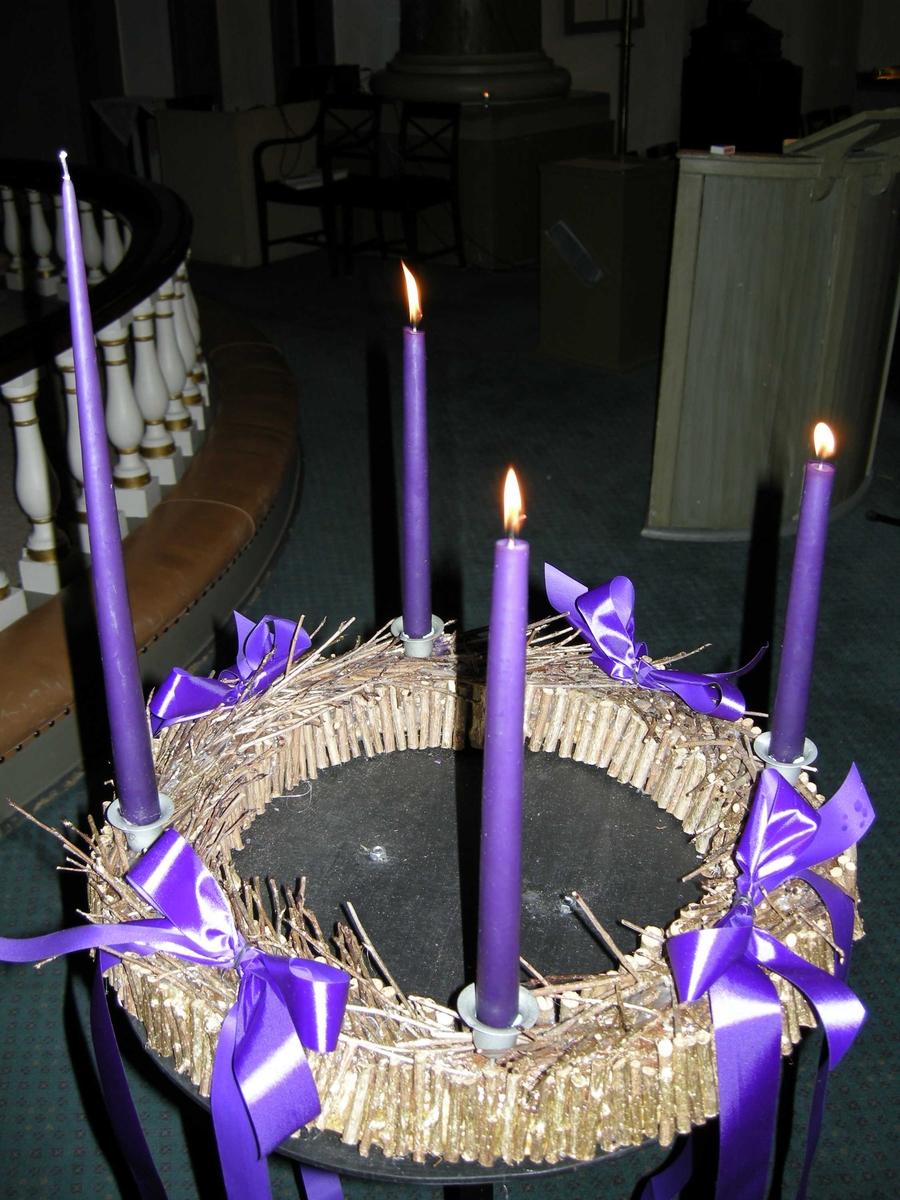 Mandal kirke tredje søndag i advent, 16.12.2007. Adventstake/adventskranse med fire lilla lys står foran alterringen. Pyntet med lilla bånd og halm. Tre lys er tent.