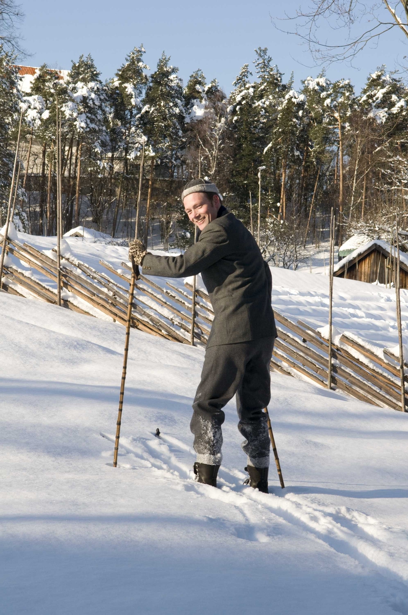 En serie med bilder av utkledd mann i klær anno 1870-1900 som går på ski på jordet bak festplassen.
Illustrasjonsfotografier.