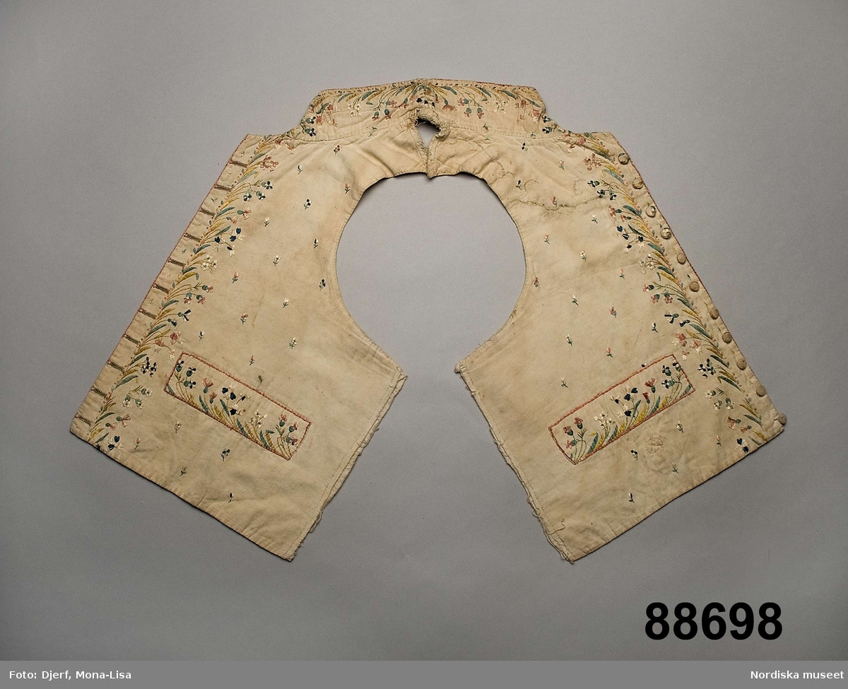 Mansväst som ursprungligen är en ren modeväst i empirmodell från tiden kring 1790-talet.  De 2 framstyckena och kragen är i vit bomullskypert och broderiet utfört i plattsöm och stjälksöm med otvinnat silke i många ljusa färger, Foder av tunn vit bomullslärft. Framstyckena går nästan ihop i nacken och i mellanrummet på 5-6 cm finns rester av  vit linnelärft som antagligen utgjort hela ryggstycket. Ståndkragen hopsydd mitt bak  efter det att broderiet gjorts. Utskuren för halsen fram så att främre delen av broderiet skurits bort., framkanterna har kunnat vikas ut som slag och är därför broderade även på insidan  högst upp. Knäppning med 11 tygklädda knappar med liten broderad blomma, alla olika. Knapphål tränsade med ljusgrönt silke med omgivande kant i rosa. De broderade ficklocken är fastsydda runtom  och har ingen fickfunktion. 
Anm. framstyckena solkiga, en lång reva och några mindre på höger sida har lagats och längre ned under ficklocket är en liten lapp av samma tyg infälld. Broderiet välbevarat.
Det är inte omöjligt att detta modeplagg från 1700-talets slut kan ha använts som brudgumsväst i Värmland 30-40 år senare. Kläder hade en lång omloppsbana och mycket begagnade kläder såldes på auktioner och marknader eller via annonser. Den bondson från Sjöbråten som hittade denna väst blev säkert lycklig över ett så fint plagg till sitt bröllop.
/Berit Eldvik 2011-05-13