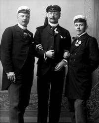 Gruppeportrett, tre menn arm i arm, med lue. Studentlue, og 