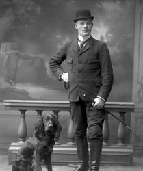 Gruppeportrett, mann i rideklær og en fuglehund.