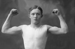 Portrett, mann i undertrøye viser muskler, strammer biceps. 