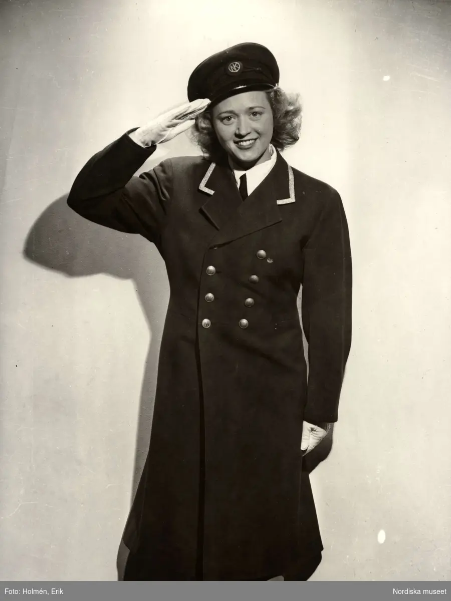 Kvinna i NK-uniform gör honnör. Nordiska Kompaniet i Stockholm.