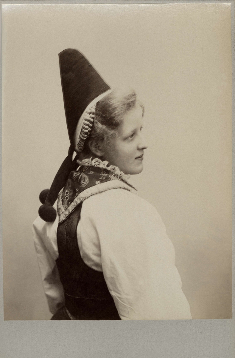 Porträtt på en kvinna i folkdräkt från Dalarna med toppig huvudbonad. Dräkt från Rättvik eller Boda i sent utförande från omkr. 1900.