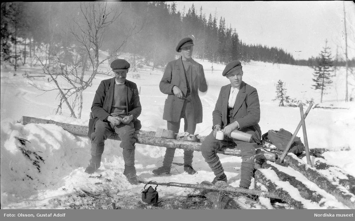 Tre män har matpaus ute på vintern. 1900-talets första hälft.