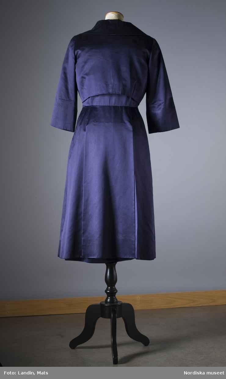 Klänning med jacka, "ambassadörsdräkt", av mörkblå sidenatlas. Sydd vid Märthaskolan 1955 efter modell från Dior. Buren av ambassdör Alva Myrdal. Nordiska museet inv nr 285285.