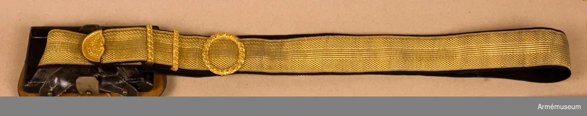 Av en 45 mm bred guldgalon m/1895. Remmen är fodrad med blått kläde. Sammanhållen av förgyllda ciselerade beslag. I ändarna anordningar av läder att fästas i kartuschlådan. Har tillhört Gustav VI Adolf (1882-1973).
