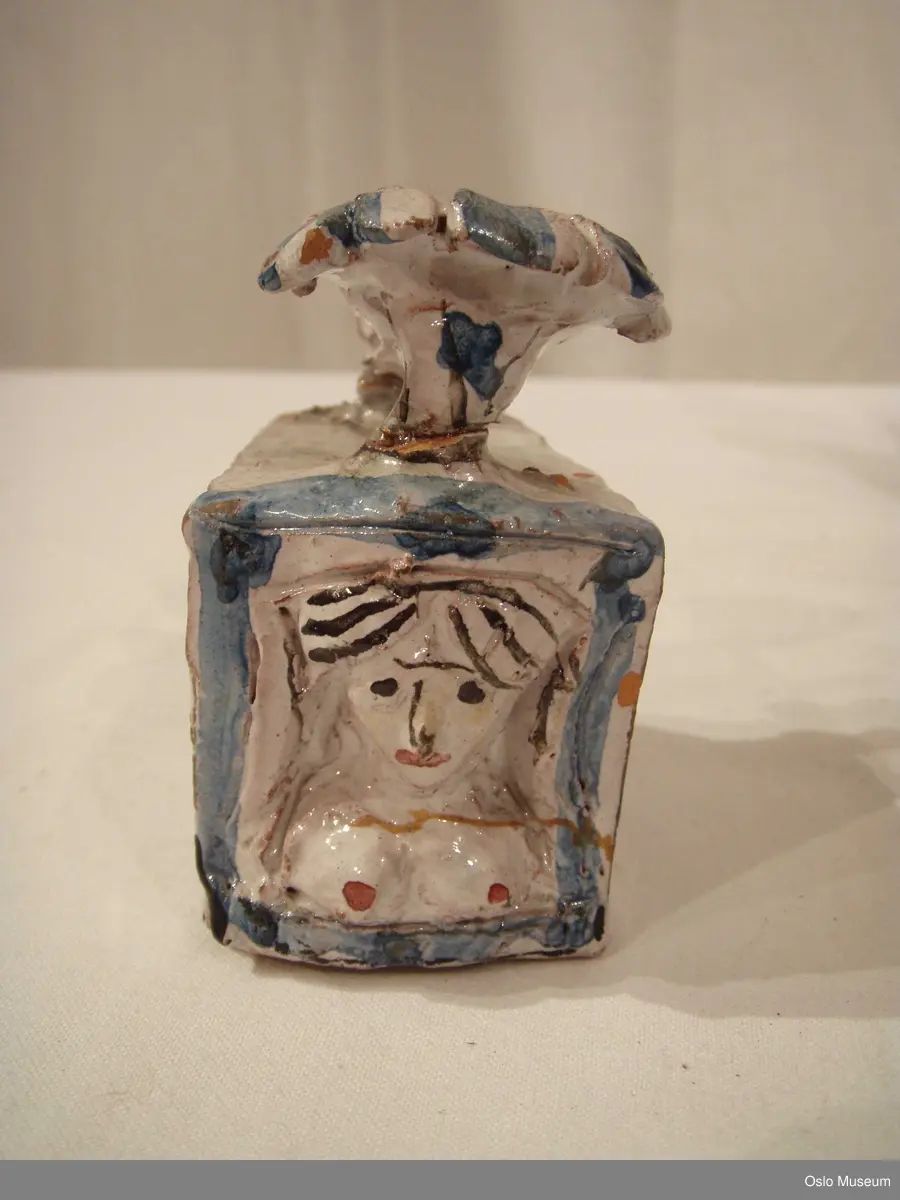 Scenografimodell av keramikk. Glasert i hvit bunnfarge med dekor/detaljer i blått og gult. 7 deler. Spesiallaget oppbevaringseske.