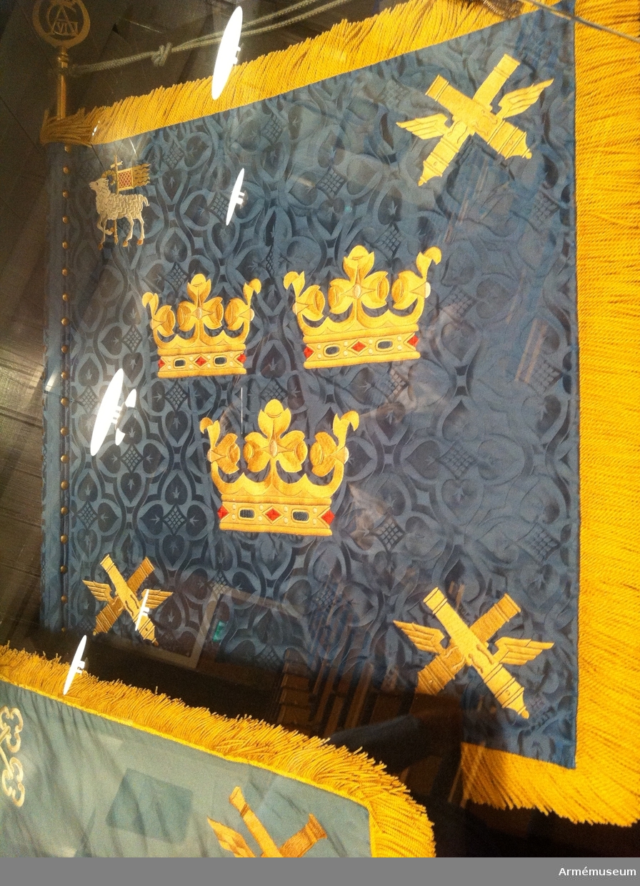 På ljusblå duk i mitten tre gula öppna kronor, i övre inre hörnet landskapet Gotlands vapenbild, i de övriga hörnen två korslagda gula bevingade eldrör av äldre modell. Gul frans. Dekor i infällning och brodyr.

Duken spikad med 59 st tännlikor.