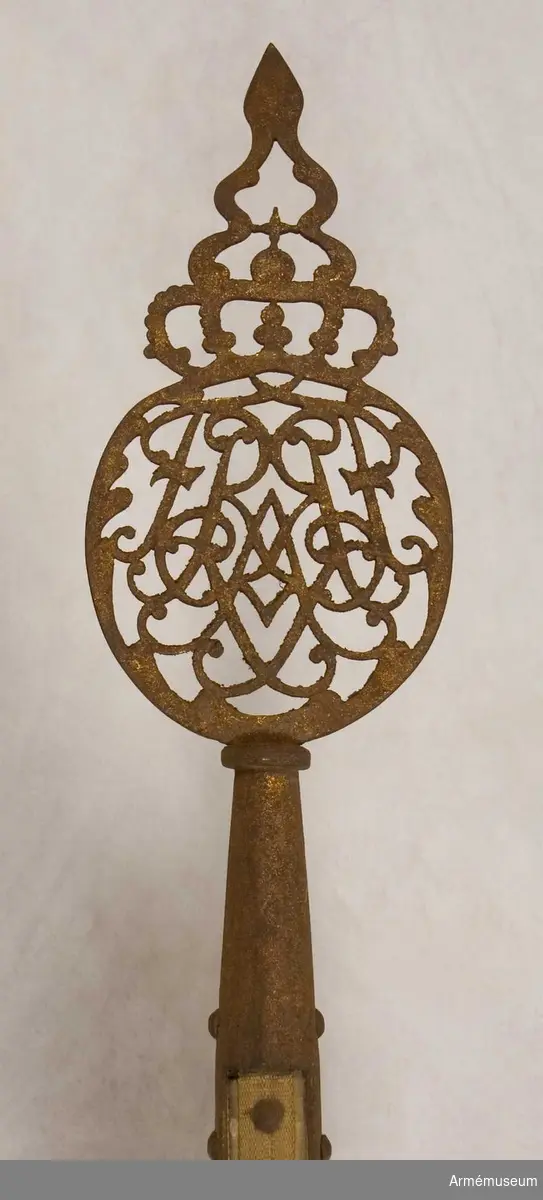 Fredrik August I:s krönta spegelmonogram omringat av två palmkvistar. Fanspets med kungens monogram.