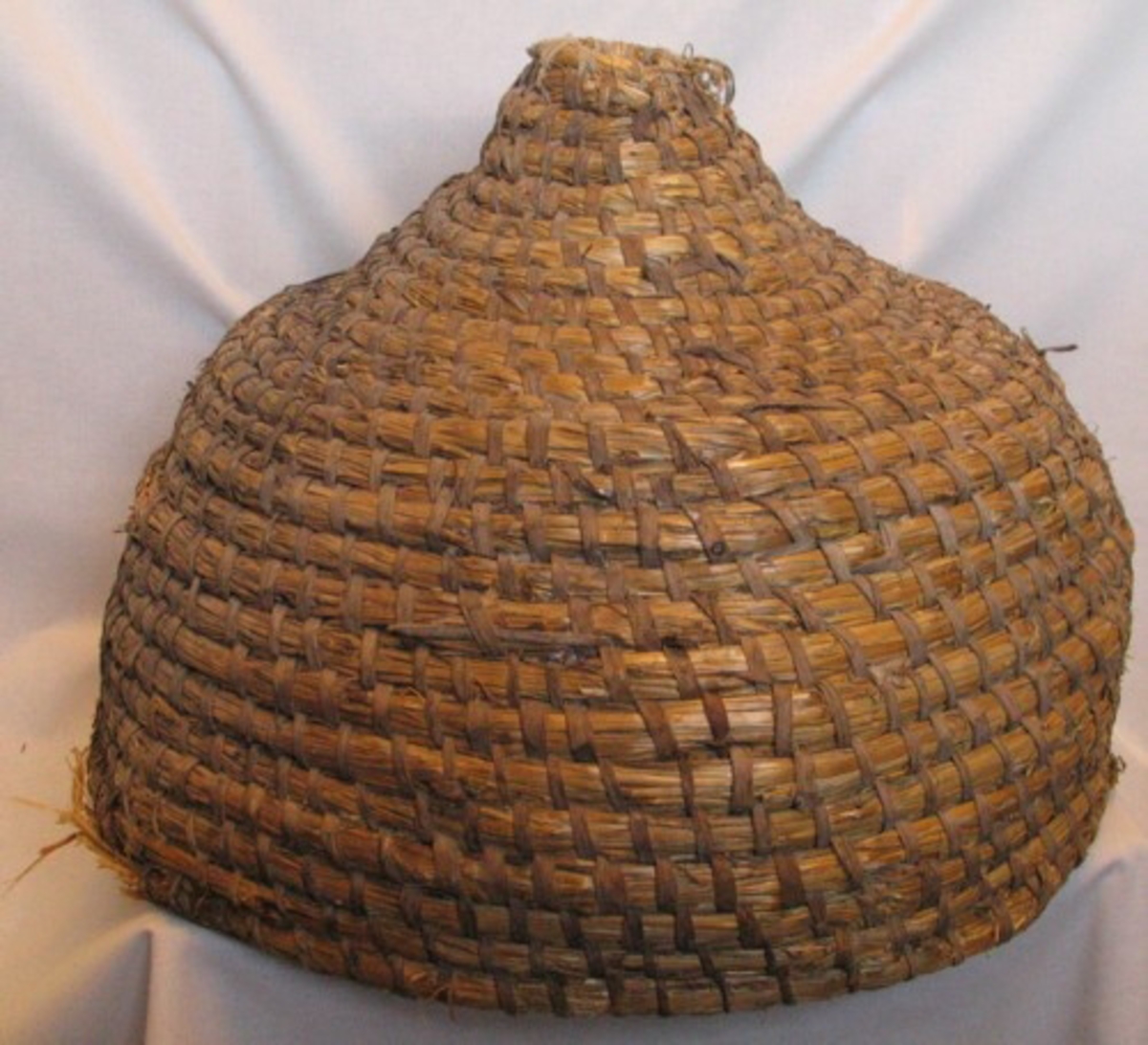 Stor kupolformad bikupa, bunden av halm med asp(?) i löbteknik. Ingångshålet(?) upptill är lagat eller tillsytt med bomullssnöre.