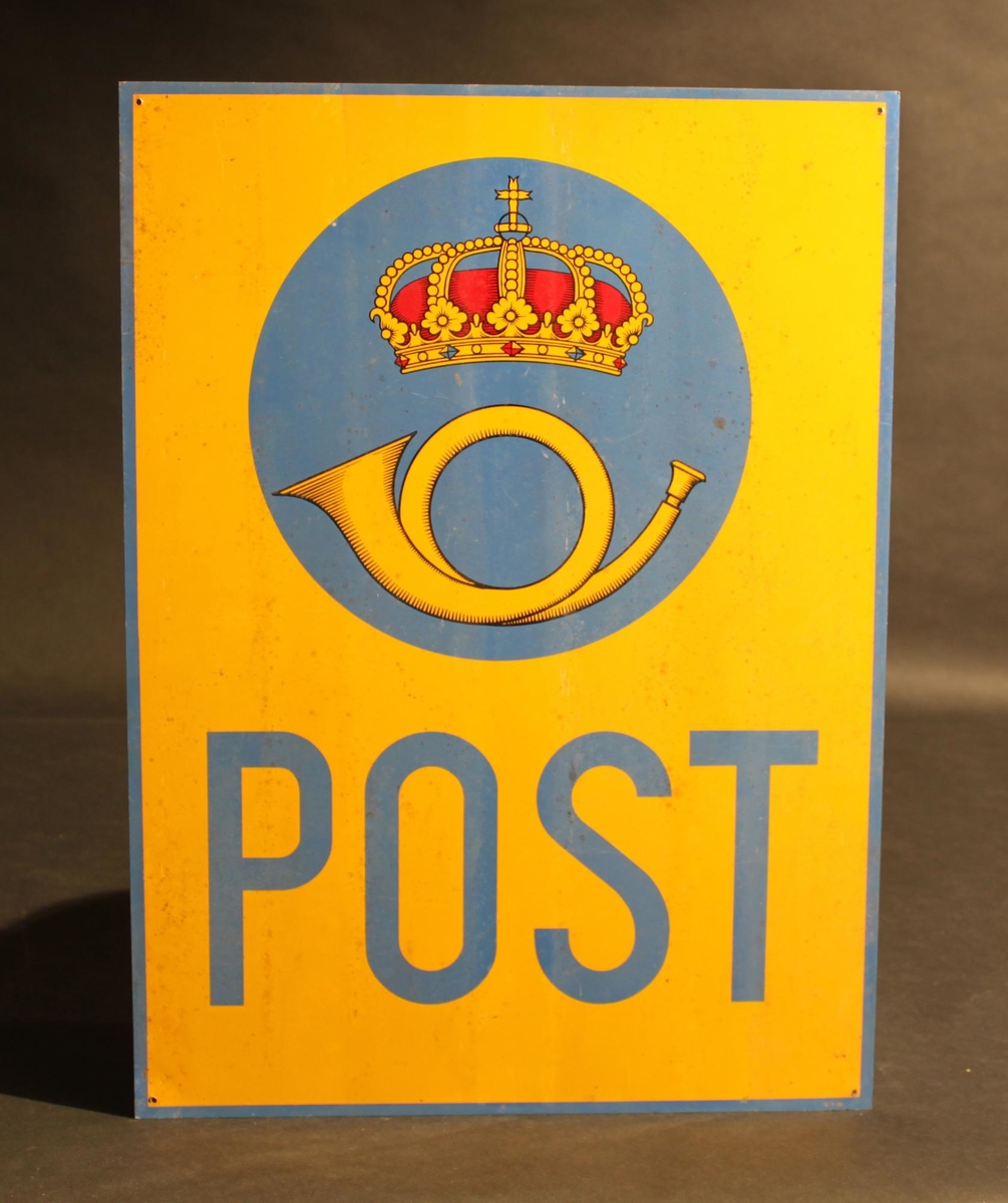 Poststationsskylt, rektangulär, tillverkad ilackerad aluminiumplåt med text "POST" i blått underst, samt ett krönt postemblem av 1937 års modell i ett cirkulärt blått fält. Skylten hargul bottenfärg , och blå kanter. I hörnen finns hål för fastsättningav skylten. Postemblemet ritat av Olle Hjortzberg. Skylten använd på poststationen i Sörmark, Värmland.