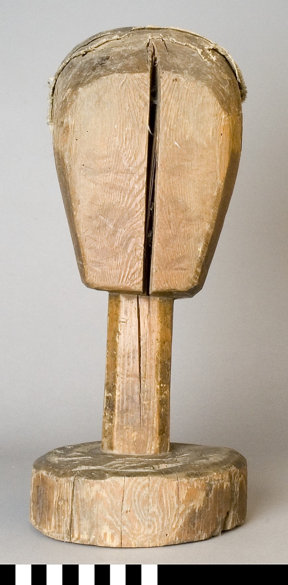 Mösstock av furu. Skulpterat huvud med rakt fäste och rund sockel. Överdelen har lager på lager med klistrad linnelärft och paper.