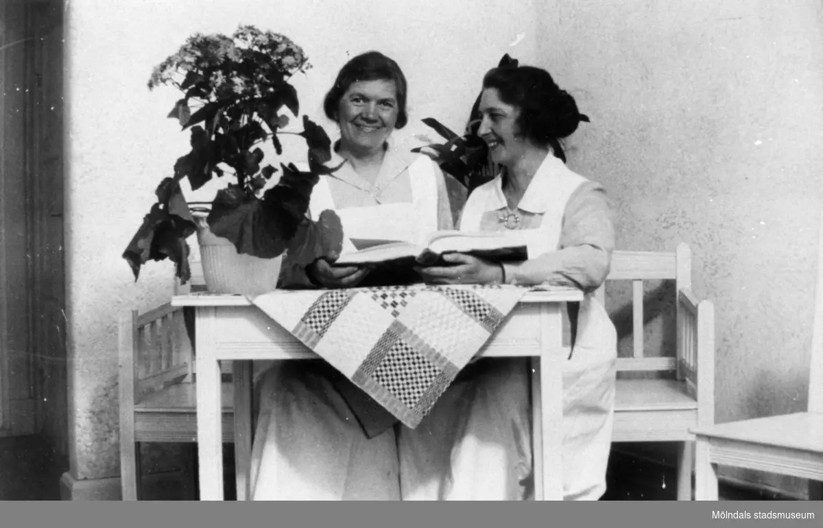 Två kvinnor sitter vid ett bord och tittar i en bok, Stretereds skolhem, cirka 1930.