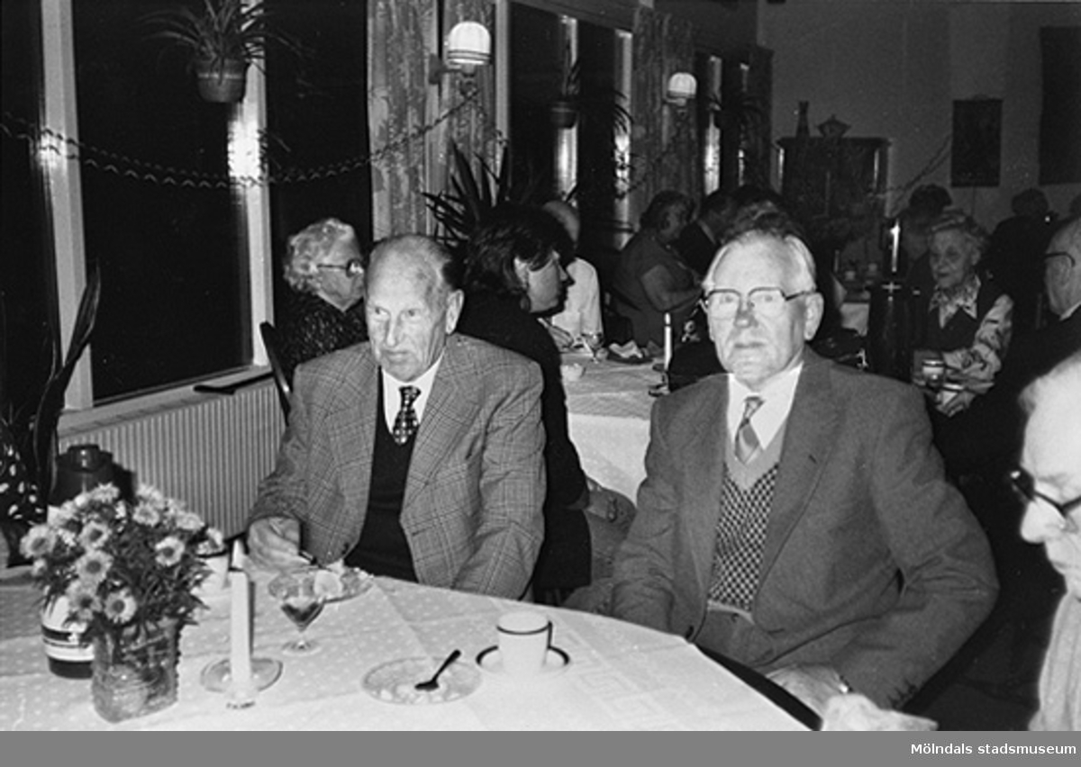 Två välklädda män sitter och dricker kaffe med avec. I bakgrunden sitter fler boenden vid andra bord. Okänt årtal.